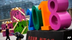 Seorang pria mendorong troli berisi bermacam barang melewati dekorasi bertuliskan “Bisnis Makmur dan Tumbuh Besar” di luar pusat perbelanjaan baju retail dan grosir di Beijing, 9 Juli 2018.
