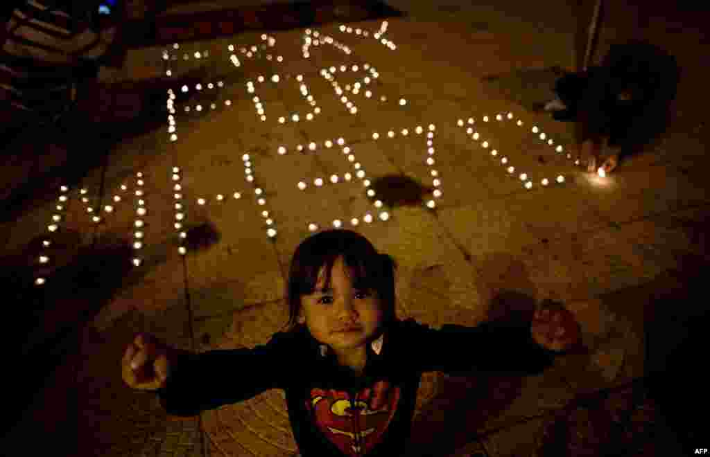 Seorang anak berpose ketika yang lainnya menyalakan lilin sambil menunggu berita tentang penumpang Malaysia Airlines yang hilang di Lapangan Kemerdekaan di Kuala Lumpur, 10 Maret 2014.