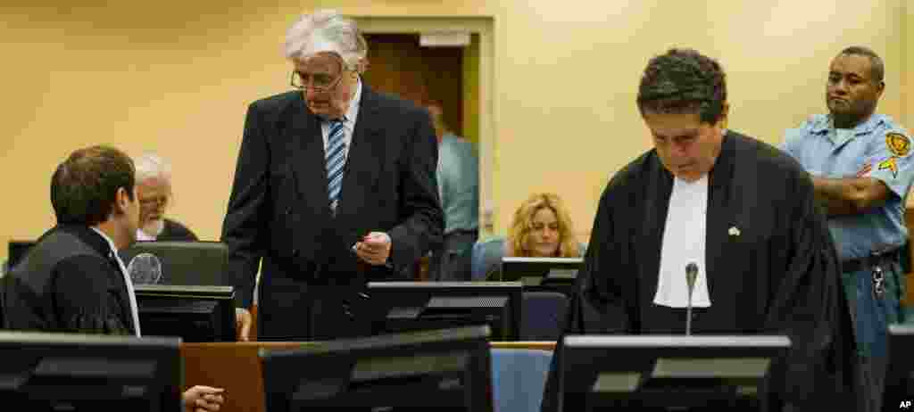 Radovan Karadzic, standing at left, talks to Marko Sladojevic, left, a member of his legal team while his legal advisor Peter Robinson, right, prepares ahead of the start of Karadzic's defense.