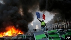Seorang pengunjuk rasa melambaikan bendera Perancis ke arah barikade yang terbakar di depan Champs-Elysees, Paris. (24/11).