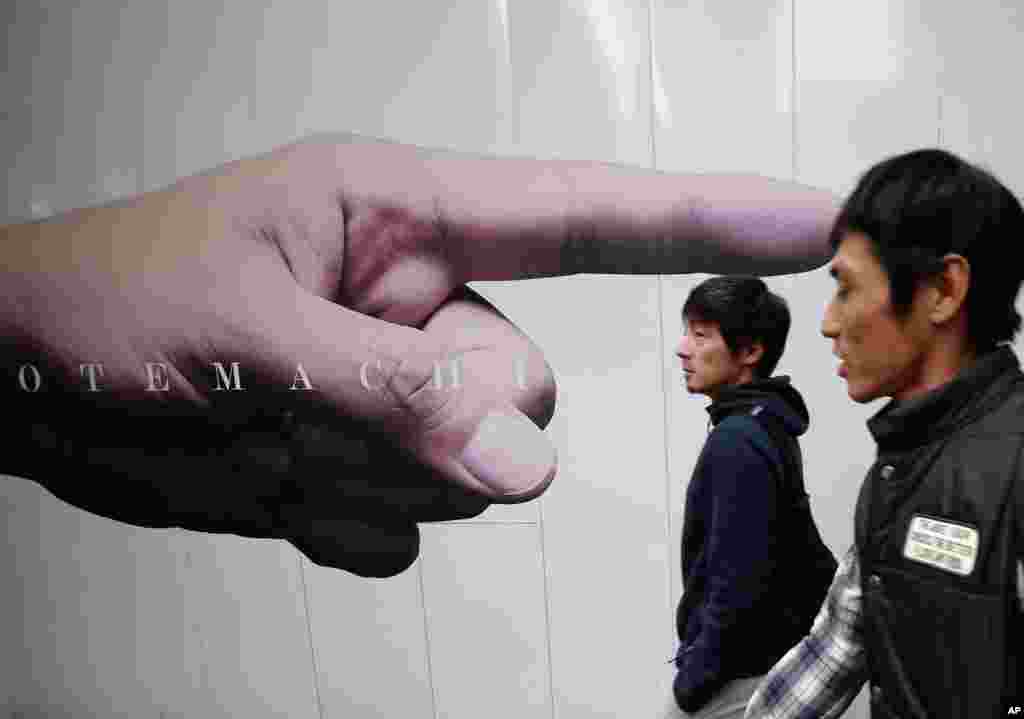 Men pass an advertisement posted on the fence of a construction site in Tokyo's Otemachi business district, Japan.