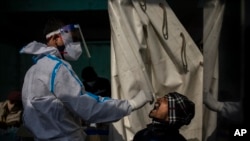 Petugas kesehatan mengambil sampel swab penumpang untuk tes COVID-19 di stasiun kereta api di New Delhi, India, Kamis, 30 Desember 2021. (Foto: AP/Altaf Qadri)