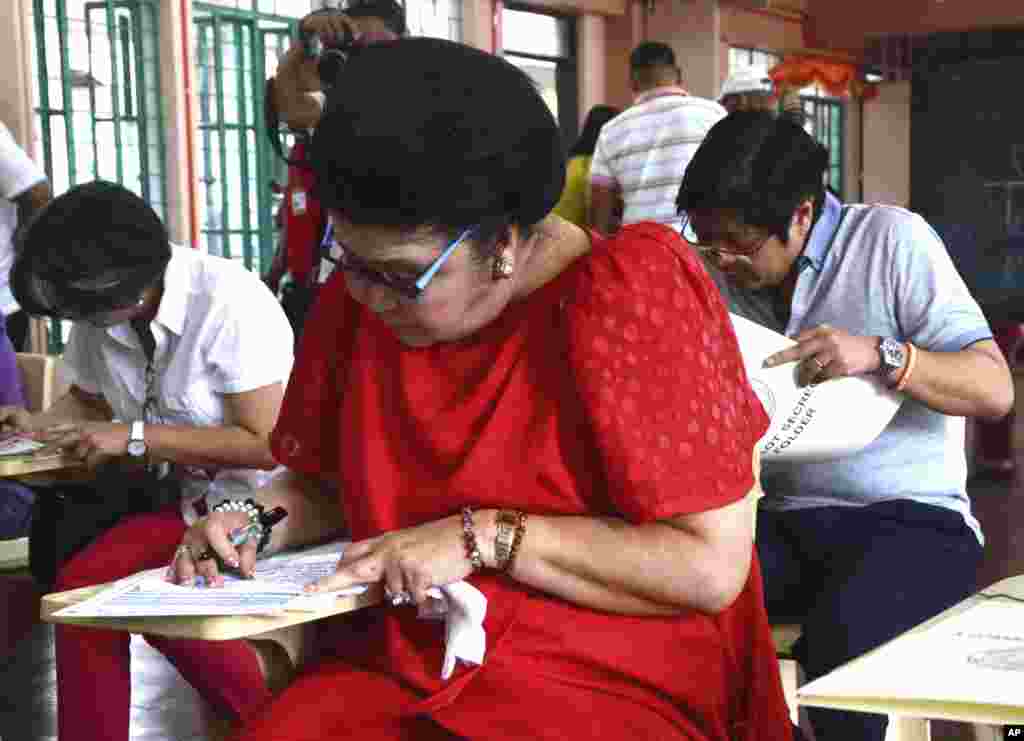 Former Philippine first lady Imelda Marcos fills out her ballot near her children Senator Ferdinand Jr. "Bongbong" Marcos and Irene Marcos Araneta in Batac, Illoos Norte, May 13, 2013.