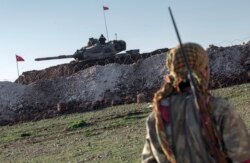 FILE - A Syrian Kurdish militia member of the YPG patrols near a Turkish army tank in Esme village in Aleppo province, Syria, Feb. 22, 2015.