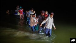 Porodice migranata, uglavnom iz zemalja Srednje Amerike, koračaju kroz vodu nakon što su ih krijumčari isporučili na malim splavovima na napuhavanje na tlo SAD-a u Romi, Teksas, 24. marta 2021. godine.