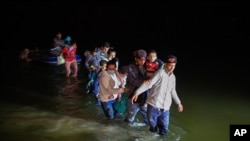 Migrant families, mostly from Central American countries, wade through shallow waters after being delivered by smugglers on small inflatable rafts on U.S. soil in Roma, Texas, March 24, 2021.