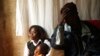 An HIV-AIDS patient (R) places her hand on her forehead during a visit by a caregiver at her home in Matero township on the outskirts of Lusaka, Zambia, April 17, 2012.