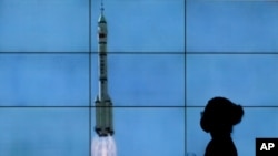 A woman wearing a face mask is silhouetted as she walks by a TV screen showing the Long March-2F Y12 rocket carrying a crew of Chinese astronauts in a Shenzhou-12 spaceship as it lifts off, in Beijing, June 17, 2021.