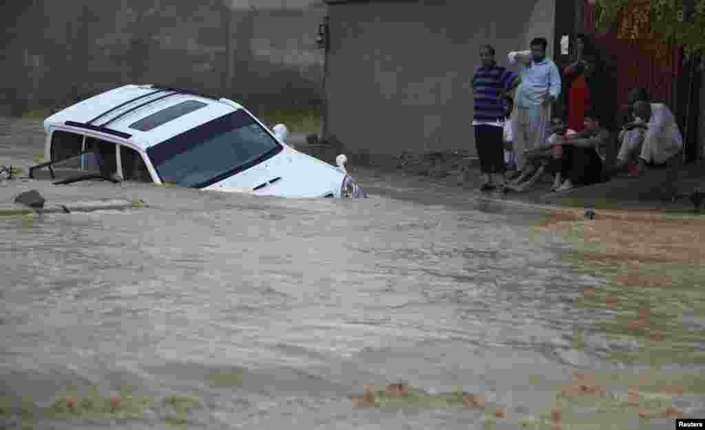 Family members wait for rescue workers after their vehicle was submerged in flood waters on the outskirts of Karachi, August 4, 2013. 