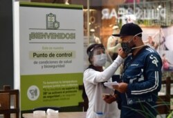 In this June 9, 2020, photo, a nurse measures the body temperature of a shopper at the El Tesoro mall, amid the new coronavirus pandemic, in Medellin, Colombia.