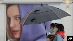 People wear masks to protect against coronavirus as they pass a shop in London, Wednesday, Feb. 3, 2021. Britain's Health Secretary Matt Hancock said Wednesday a new study suggesting that a single dose of the AstraZeneca vaccine may reduce transmission of COVID19.