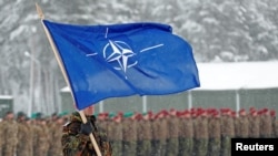 Seorang tentara membawa bendera NATO di pangkalan militer Rukla, Lituania 4 Februari 2019. (Foto: REUTERS/Ints Kalnins )