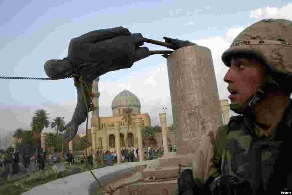U.S. Marine Corp Assaultman Kirk Dalrymple watches as a statue of Iraq's President Saddam Hussein falls in central Baghdad, April 9, 2003.