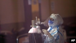 A health worker fixes an oxygen cylinder for a COVID-19 patient at a banquet hall converted into a quarantine center ,in New Delhi, India, Friday, April 23, 2021.