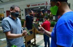 In this June 8, 2020 photo, an El Tesoro mall employee uses his mobile to scan a customer's app to verify he is registered for entry, in Medellin, Colombia, June 8, 2020.