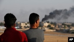 People standing on a rooftop in Akcakale, Sanliurfa province, southeastern Turkey, at the border with Syria, watch as in the background smoke billows from fires caused by Turkish bombardment in Tal Abyad, Syria, Sunday, Oct. 13, 2019. Turkey's…