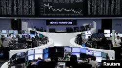 FILE - Traders work at their desks in front of the German share price index, DAX board, at the stock exchange in Frankfurt, Germany, Feb. 16, 2016.