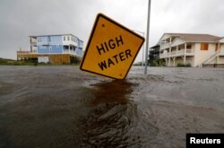 El agua casi alcanza una señal de alerta de inundación parcialmente doblada por el huracán Florence en Oak Island, Carolina del Norte, el 15 de septiembre de 2018.