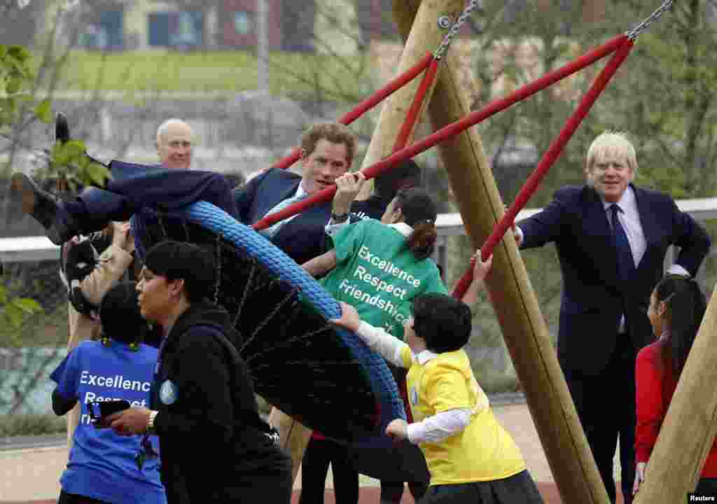 Britain's Prince Harry plays on a swing with children as Mayor of London Boris Johnson (R) looks on during a viewing of Queen Elizabeth Olympic Park ahead of its opening on April 5, 2014, at Stratford in east London.