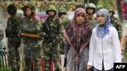 Dua perempuan etnis Uighur melewati polisi paramiliter China yang berjaga di luar Grand Bazaar di distrik Uighur di kota Urumqi di wilayah Xinjiang China pada 14 Juli 2009. (Foto: AFP/Peter Parks)