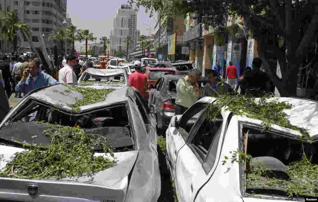People walk on a street lined with a damaged building and destroyed cars after a blast at Marjeh Square in Damascus, April 30, 2013.