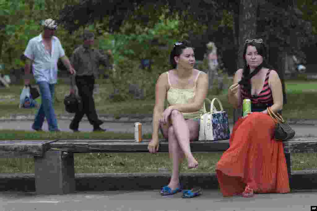 Para perempuan menikmati udara hangat di alun-alun pusat kota Slovyansk, Ukraina timur (19/5). (AP/Alexander Zemlianichenko)