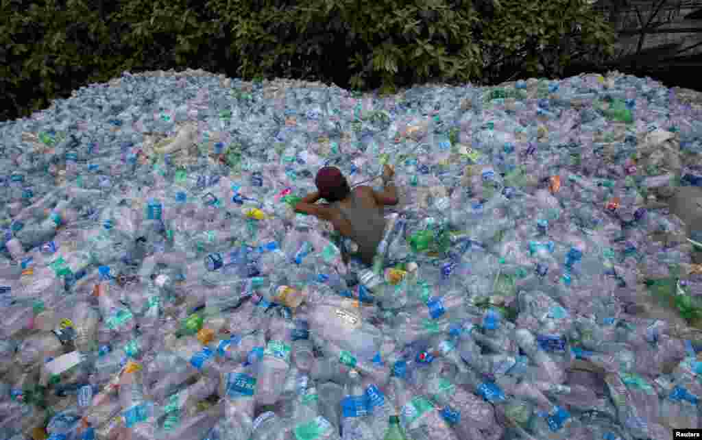A worker uses a rope to move through a pile of empty plastic bottles at a recycling workshop in Mumbai, India.