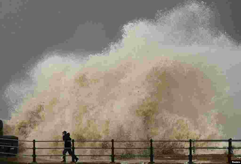 A woman is sprayed by a wave as she walks along the seafront in New Brighton, England.