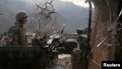 An Afghan National Army (ANA) soldier is seen through damaged glass as he keeps watch at the Forward Base in Nari district near the army outpost in Kunar province, Feb. 24, 2014