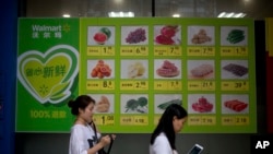 Orang-orang berjalan melewati papan reklame yang menampilkan harga jual produk segar di luar toko Walmart di Beijing, China, 19 Juli 2018. (Foto: dok)