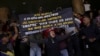 Un manifestante sostiene un cartel que exige mejores salarios mientras los partidarios del gobierno se paran detrás en un intento de que los manifestantes abandonen el Ministerio de Trabajo en Caracas, Venezuela, el miércoles 15 de marzo de 2023. (Foto AP/Matías Delacroix)