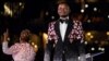 FILE - Pastor Shepherd Bushiri, right, from the Enlightened Christian Gathering stands on stage while his wife speaks to worshippers at the FNB Stadium in Soweto, Jan. 1, 2020.