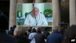 Ljudi gledaju u džinovski ekran na Trgu Svetog Petra u Vatikanu, na kojem se vidi papa Franjo kako čita podnevnu molitvu Anđela iz svoje rezidencije, nakon što je odlučio da se ne pojavi lično na prozoru svog studija zbog uporne prehlade, 22. decembra. 2024.