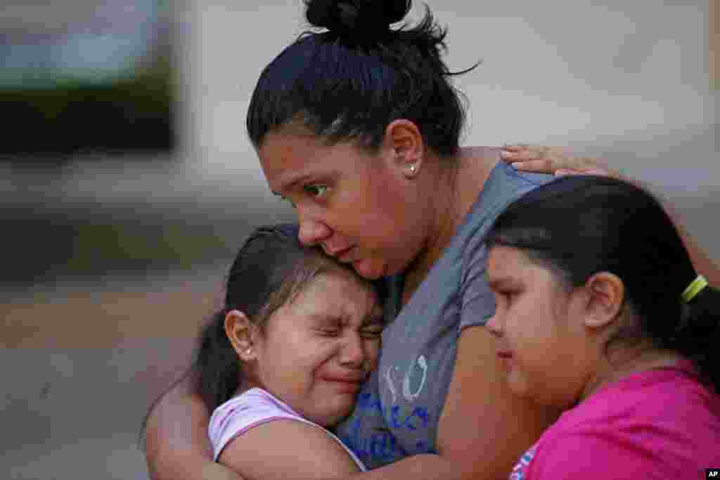 Seorang ibu menenangkan dua putrinya yang menangis di memorial untuk menghormti para polisi Dallas, di depan kantor polisi kota itu (9/7). (AP/Gerald Herbert)