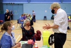 Britain's Prime Minister Boris Johnson speaks with a woman waiting to receive an Oxford-AstraZeneca COVID-19 vaccine, during his visit at a vaccination center at Cwmbran Stadium in Cwmbran, south Wales, Britain, Feb. 17, 2021.