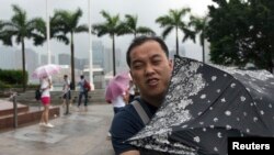 Seorang pria berusaha menahan terpaan angin dengan payungnya di Lapangan Golden Bauhinia, saat topan Utor mendekati Hong Kong (14/8).