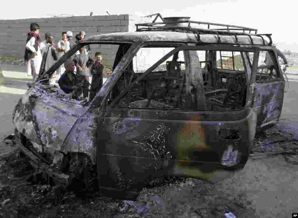 Men investigate the remains of a burnt vehicle after a suicide attack in Ghazni Province, Afghanistan, August 29, 2013.