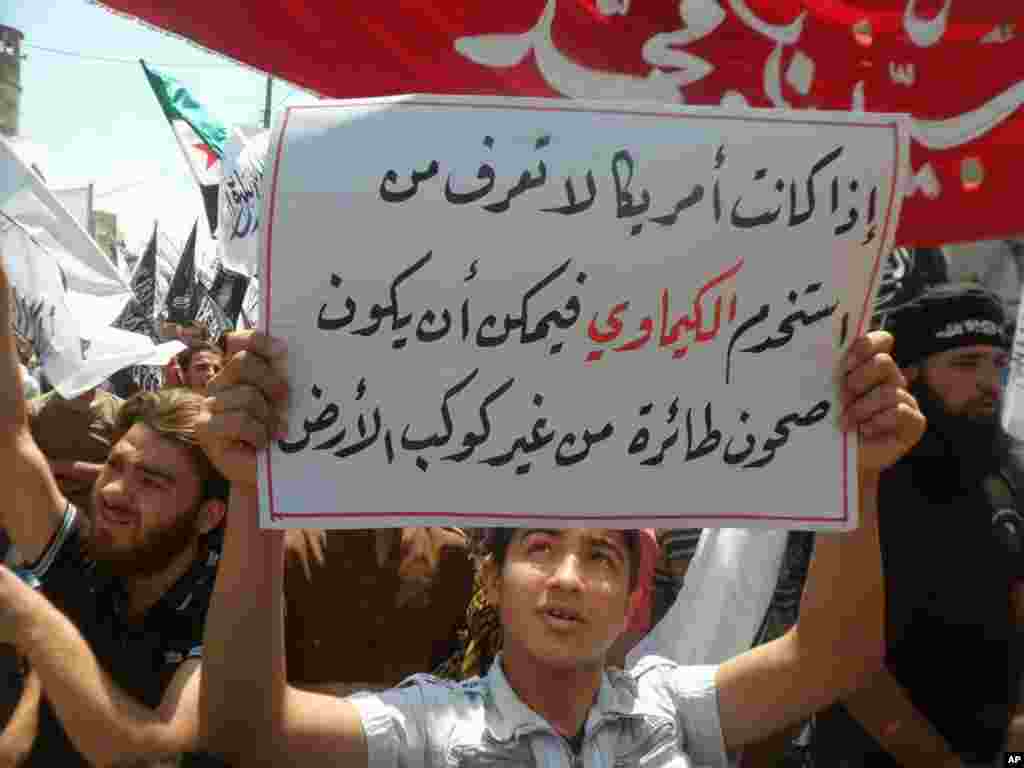 This image provided by ENN shows a protester with a sign reading "If America does not know who used the chemical weapons, so it could be flying saucers from another planet," Sarmada, Idlib, Syria, May 3, 2013.