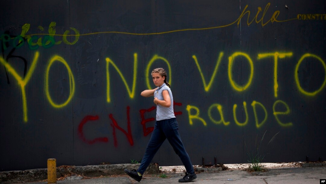 Una transeúnte pasa frente a un grafitti en Caracas que censura la elección presidencial del 20 de mayo, califcándola de fraude.