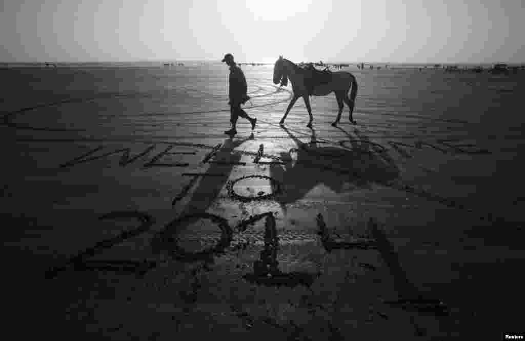 A man leads his horse past a message left by a visitor on New Year's Eve, along Clifton Beach, Karachi, Pakistan, Dec. 31, 2013. 