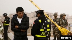 在中國新疆維吾爾自治區喀什的一條街上，警察檢查一名男子的身份證，旁邊有安全人員。(2017年3月24日)