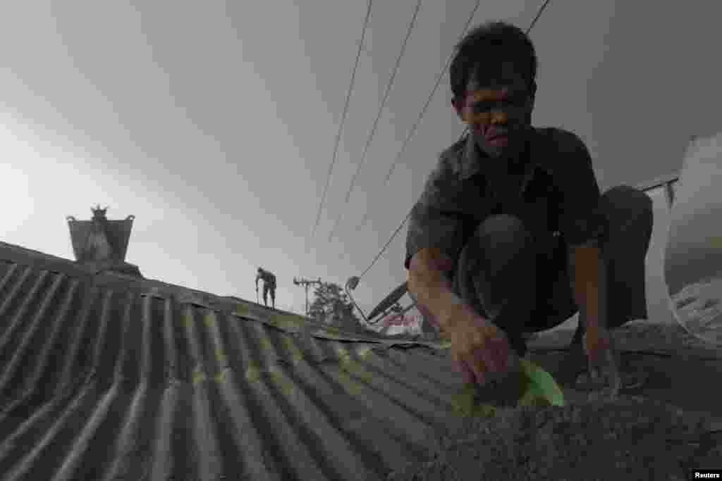 Para penduduk desa membersihkan atap rumah mereka dari abu yang berasal dari letusan Gunung Sinabung seperti terlihat di desa Sibintun di Karo, Indonesia, 14 Januari 2014. 