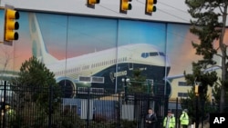 FILE - Workers exit the Boeing factory in Renton, Washington, where the company's 737 Max airplanes are built, with a painted exterior door of the factory in the background, Dec. 17, 2019. 