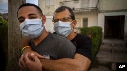 Lázaro “Lachi” González, behind, hugs his partner Adiel González after a video interview outside their home in Matanzas, Cuba, Thursday, Oct. 7, 2021. (AP Photo/Ramon Espinosa)