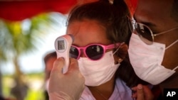 A little girl wearing a face mask amid the new coronavirus pandemic gets her temperature taken at a police checkpoint, at the entrance to the province of Havana, Cuba, Aug. 10, 2020.