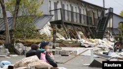 Mahasiswi beristirahat di depan gedung apartemen yang hancur akibat gempa bumi di kota Minamiaso di prefektur Kumamoto, Jepang selatan (16/4). 