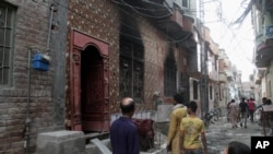 FILE - Residents look at the house of a family belonging to the Ahmadi sect, which was torched by angry mob in Gujranwala, Pakistan, July 28, 2014.