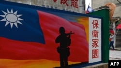 Seorang turis (kanan) berjalan melewati mural yang dilukis di dinding di Pulau Kinmen Taiwan, yang terletak hanya 3,2 km (dari pantai daratan China (di latar belakang) di Selat Taiwan, 21 Oktober 2020. (Foto: AP)