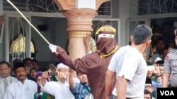 Algojo pelaksana cambuk mengayunkan rotan ke punggung pelanggar syariah di Banda Aceh, 19 September 2014. (VOA/Budi Nahaba)
