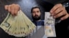 A money changer with a U.S dollar and the amount being given when converting it into Iranian rials at a currency exchange shop in Tehran's business district, January 20, 2016. 